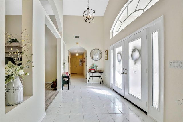 entryway with french doors, light tile patterned flooring, a high ceiling, and an inviting chandelier