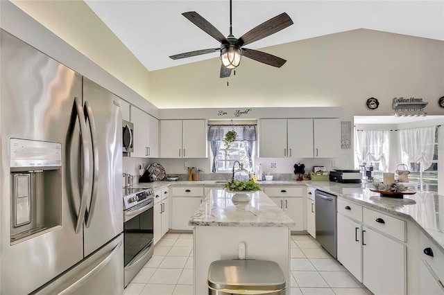 kitchen with light stone countertops, appliances with stainless steel finishes, vaulted ceiling, white cabinets, and a kitchen island