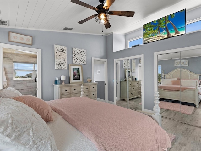 bedroom featuring ceiling fan, light hardwood / wood-style floors, multiple closets, and multiple windows