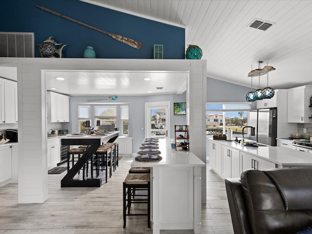 kitchen featuring pendant lighting, lofted ceiling, a kitchen island with sink, a kitchen breakfast bar, and appliances with stainless steel finishes