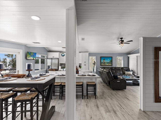 dining room with ceiling fan, vaulted ceiling, and light hardwood / wood-style flooring