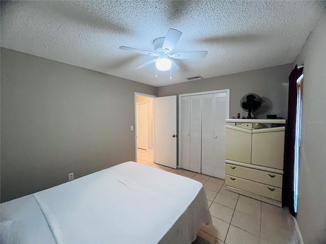 bedroom with ceiling fan, a closet, light tile patterned flooring, and a textured ceiling