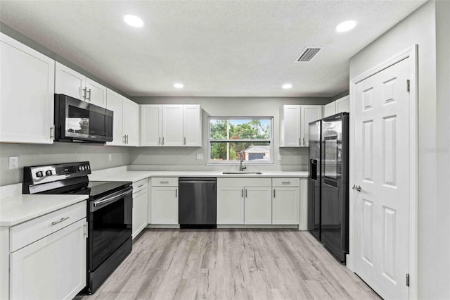 kitchen featuring light wood-type flooring, a textured ceiling, sink, black appliances, and white cabinets