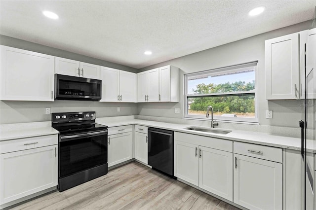 kitchen featuring sink, light hardwood / wood-style flooring, a textured ceiling, white cabinets, and black appliances