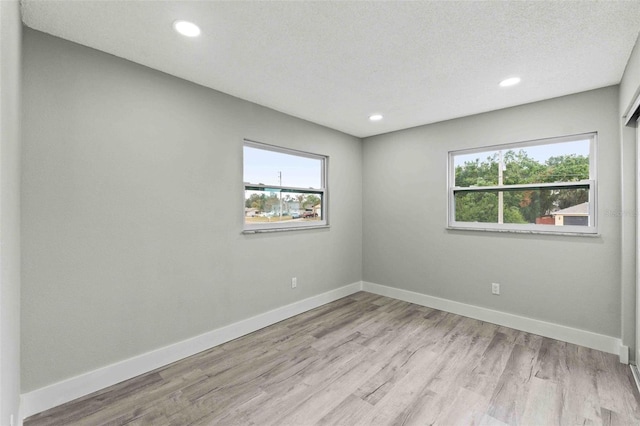 empty room with a textured ceiling, light wood-type flooring, and a wealth of natural light