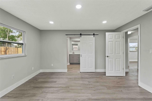 unfurnished bedroom featuring a barn door, light hardwood / wood-style flooring, ensuite bath, and a textured ceiling