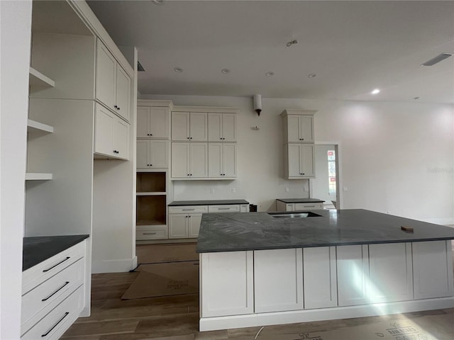 kitchen featuring white cabinets, dark hardwood / wood-style flooring, a spacious island, and dark stone counters