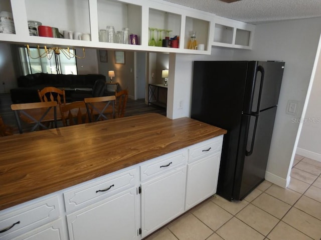 kitchen featuring butcher block countertops, light tile patterned flooring, black fridge, and white cabinets