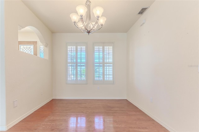 empty room featuring wood-type flooring, an inviting chandelier, and plenty of natural light