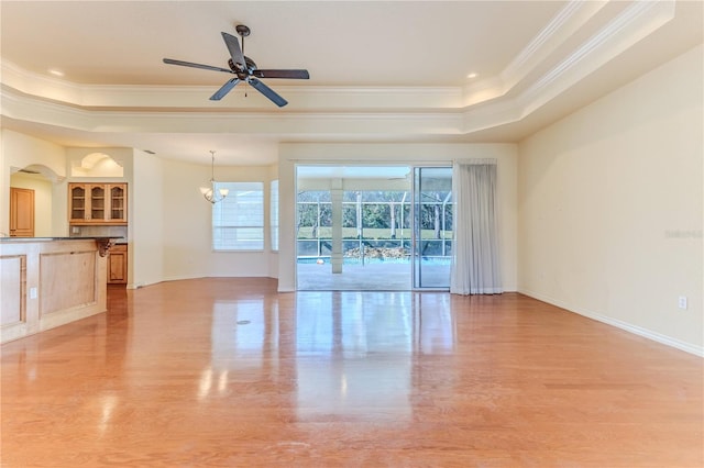 unfurnished living room featuring ceiling fan with notable chandelier, light wood-type flooring, a tray ceiling, and crown molding