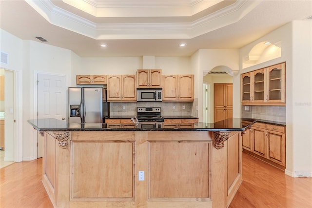 kitchen featuring a raised ceiling, backsplash, a kitchen island with sink, and appliances with stainless steel finishes