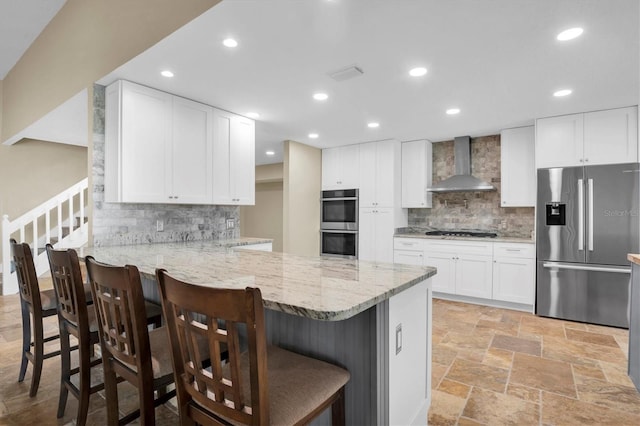 kitchen featuring a breakfast bar, white cabinets, wall chimney range hood, kitchen peninsula, and stainless steel appliances