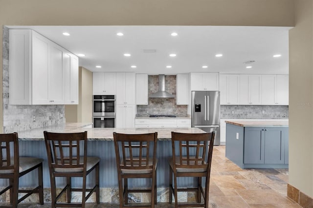 kitchen with white cabinets, appliances with stainless steel finishes, a kitchen bar, and wall chimney range hood