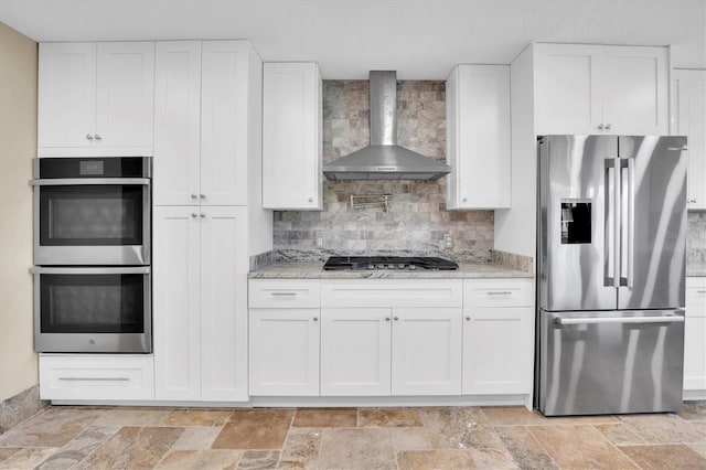 kitchen featuring appliances with stainless steel finishes, white cabinetry, and wall chimney range hood