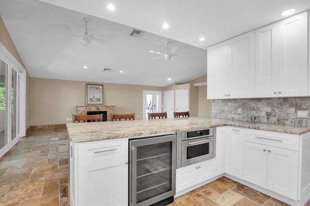 kitchen with white cabinetry, stainless steel oven, beverage cooler, kitchen peninsula, and vaulted ceiling