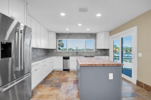 kitchen with a center island, sink, wooden counters, stainless steel refrigerator with ice dispenser, and white cabinets