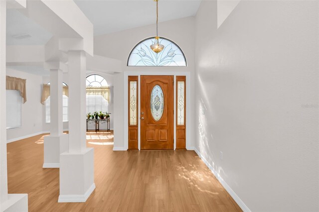 foyer with ornate columns, high vaulted ceiling, and light hardwood / wood-style floors