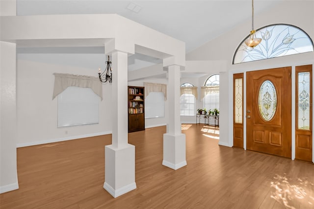 foyer with a notable chandelier, ornate columns, wood-type flooring, and vaulted ceiling