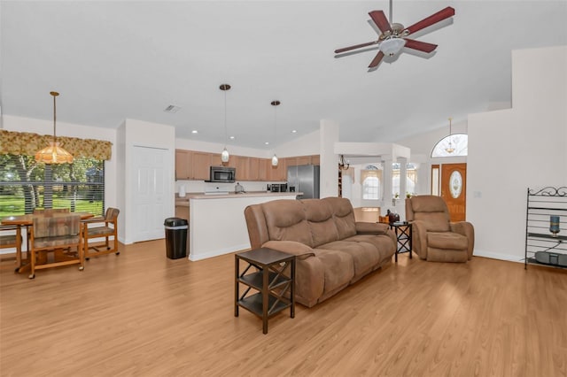 living room featuring plenty of natural light, ceiling fan with notable chandelier, light hardwood / wood-style floors, and vaulted ceiling