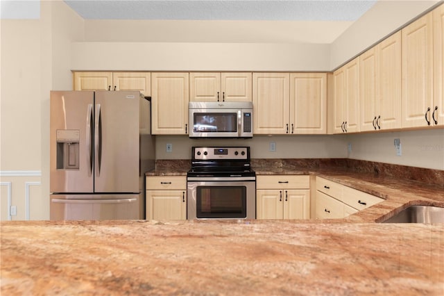 kitchen with stone counters, appliances with stainless steel finishes, and cream cabinets