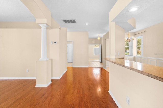 hallway with hardwood / wood-style floors, ornate columns, a textured ceiling, and an inviting chandelier