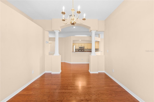 unfurnished dining area with hardwood / wood-style floors, ornate columns, and a notable chandelier