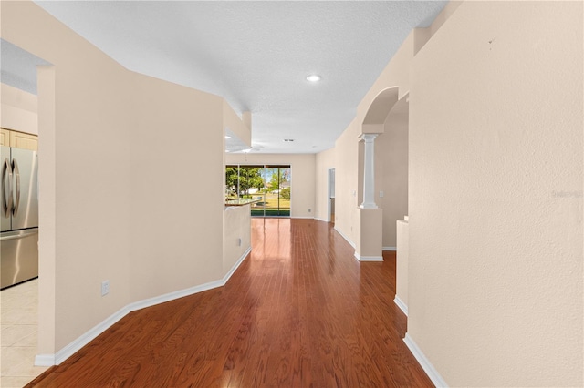 corridor with decorative columns, a textured ceiling, and light wood-type flooring