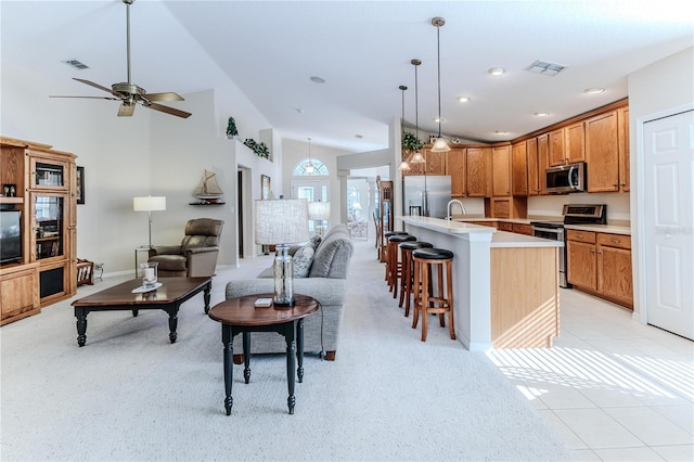 kitchen featuring a center island with sink, light tile patterned floors, appliances with stainless steel finishes, decorative light fixtures, and a breakfast bar area