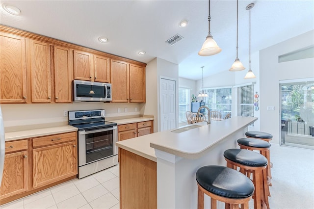 kitchen with a kitchen breakfast bar, vaulted ceiling, decorative light fixtures, a kitchen island with sink, and appliances with stainless steel finishes