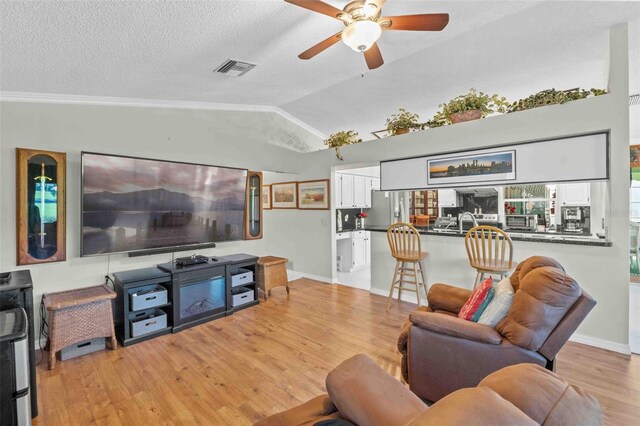 living room featuring a textured ceiling, ceiling fan, vaulted ceiling, and light wood-type flooring