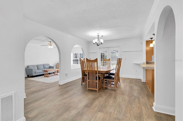 dining area with ceiling fan with notable chandelier, wood-type flooring, and a textured ceiling