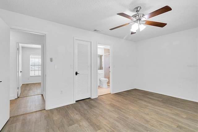 unfurnished bedroom featuring ceiling fan, light wood-type flooring, a textured ceiling, and connected bathroom