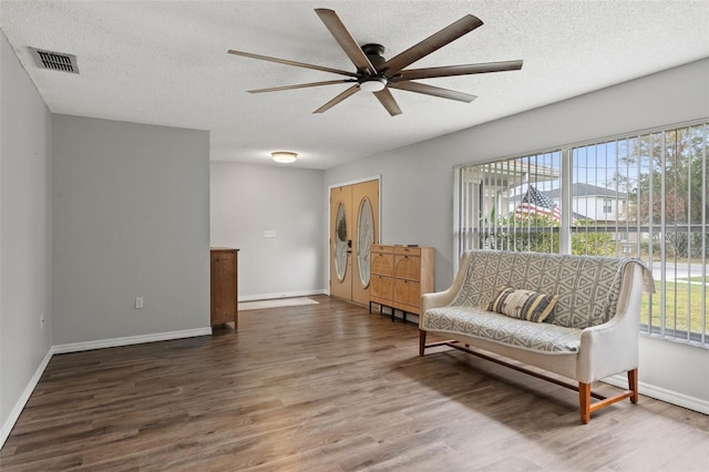 living area with ceiling fan, wood-type flooring, and a textured ceiling