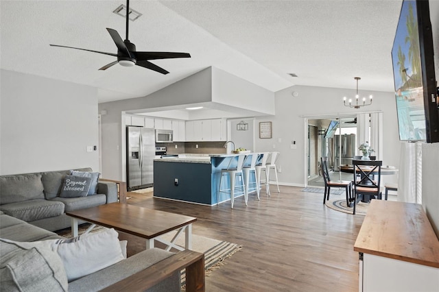 living room featuring ceiling fan with notable chandelier, a textured ceiling, sink, hardwood / wood-style floors, and lofted ceiling