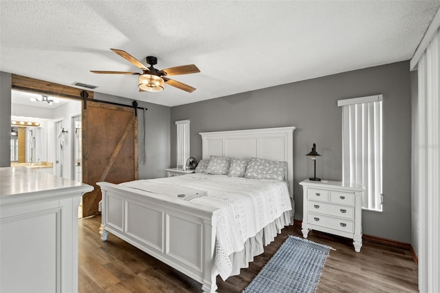 bedroom with a textured ceiling, ceiling fan, a barn door, and dark hardwood / wood-style floors