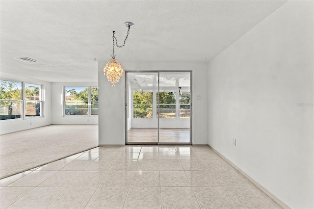 spare room with a textured ceiling, light carpet, and an inviting chandelier