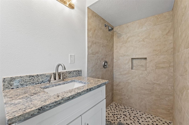 bathroom featuring vanity, a textured ceiling, and tiled shower