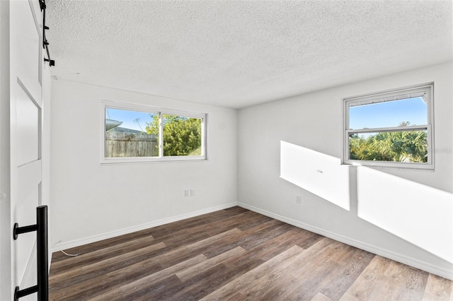 unfurnished room with a textured ceiling, a healthy amount of sunlight, and dark wood-type flooring