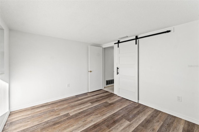 unfurnished bedroom featuring a textured ceiling, a barn door, and hardwood / wood-style flooring