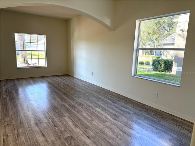 empty room featuring dark wood-style floors, arched walkways, and baseboards