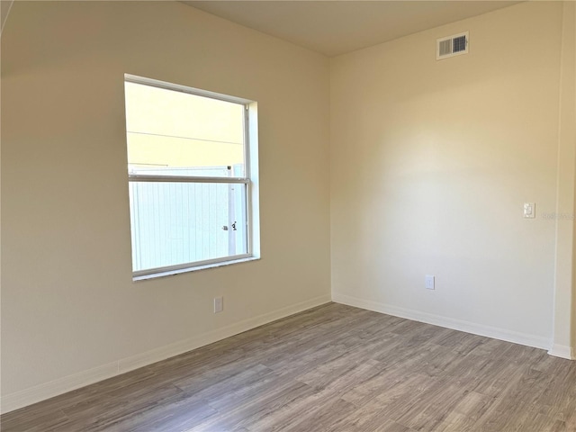 spare room with baseboards, visible vents, and wood finished floors