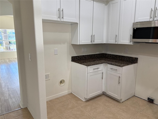 kitchen featuring light tile patterned flooring, visible vents, white cabinets, stainless steel microwave, and dark stone countertops