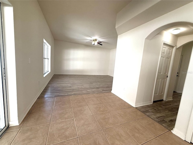 empty room featuring a ceiling fan, arched walkways, baseboards, and tile patterned floors