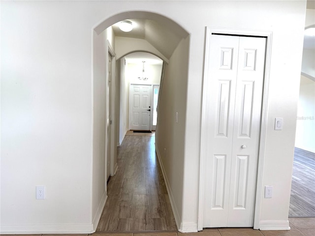 corridor featuring arched walkways, wood finished floors, and baseboards