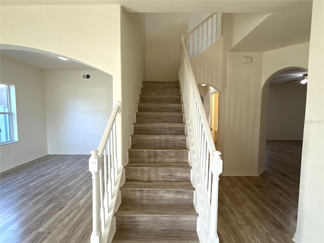 stairway with arched walkways, wood finished floors, and baseboards