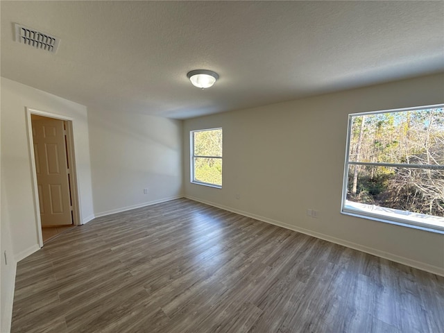 unfurnished room featuring baseboards, visible vents, dark wood finished floors, and a textured ceiling