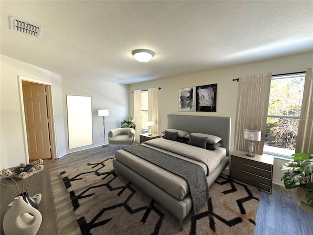 bedroom featuring wood finished floors, visible vents, a textured ceiling, and multiple windows