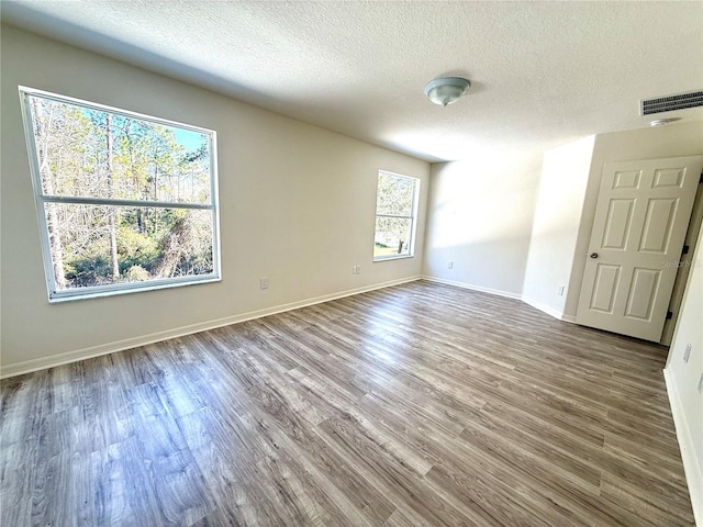 unfurnished room featuring visible vents, a textured ceiling, baseboards, and wood finished floors