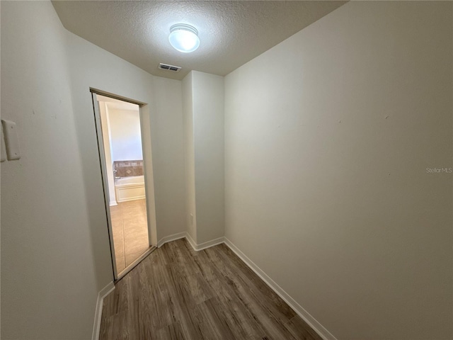 corridor featuring baseboards, visible vents, dark wood finished floors, and a textured ceiling