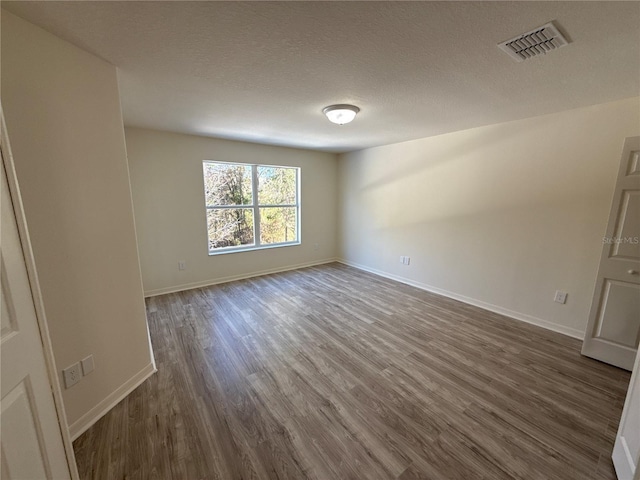 spare room with baseboards, a textured ceiling, visible vents, and dark wood-style flooring